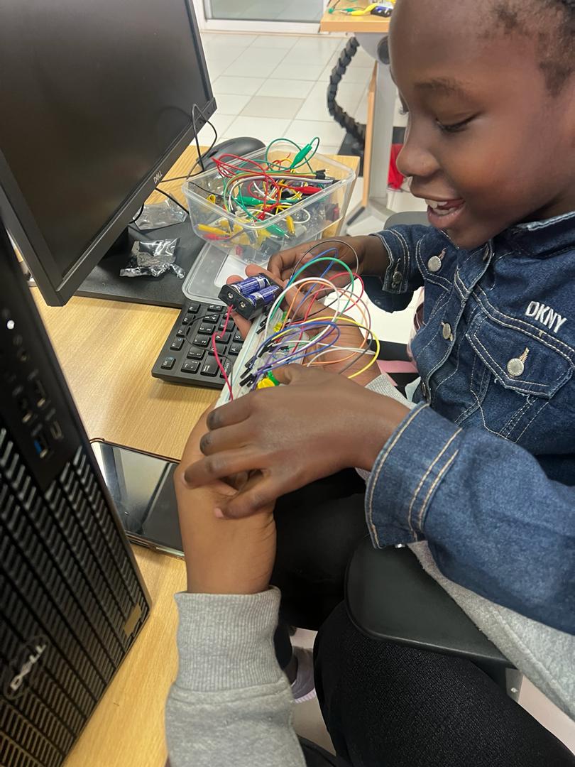A smiling learner holding the wires of a circuit she built