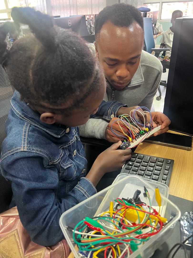 A mentor guiding a girl as she wires a robotics kit